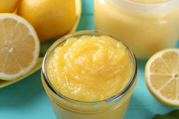 Delicious lemon curd in glass jar and fresh citrus fruits on light blue table, closeup