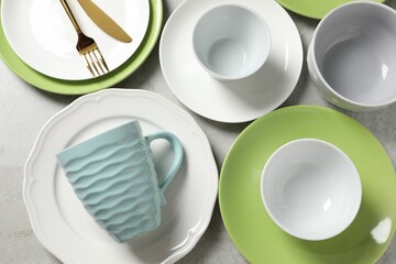 Beautiful ceramic dishware, cup and cutlery on light grey table, flat lay