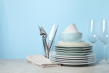 Beautiful ceramic dishware, glasses and cutlery on light grey table, space for text