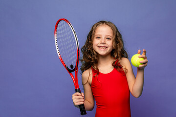 Cheerful little sports girl in red suit playing tennis isolated over lilac background. Sport, study, childhood concept. Copy space for ad, text. Beach summer tennis camp.