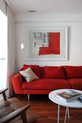 Bold and beautiful, a scarlet red sofa takes center stage in this sleek living room, accented by a minimalist white frame on the wall, ready to showcase artistry.