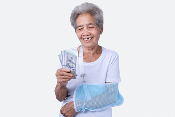 A sen woman with broken arm and wearing a sling with a smiling face and holding dollars for insurance and paid care isolated on a white background. Old elderly female medical care. Health care concept © maemodnit13