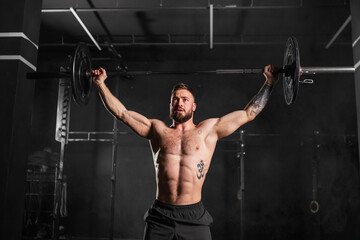 Strong man performing overhead squat pressing barbell up, waist up shot. Routine workout for...