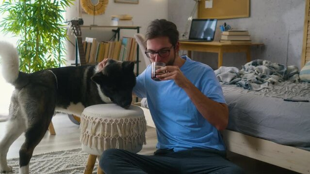 Smiling young man enjoying drinking his morning coffee spending time with his pet in the bedroom. Waking up routine 