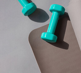 Sport or workout concept flat lay with blue dumbbells, yoga mat on the grey background. Copy space