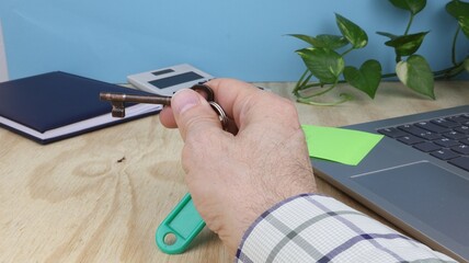 La mano dell'uomo tiene una chiave, sulla scrivania dell'ufficio immobiliare con computer e post-it.