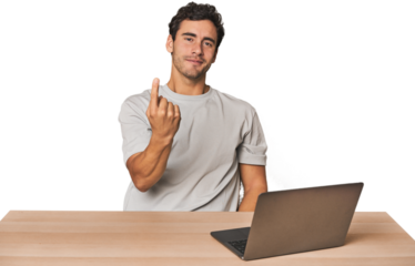 Hispanic young man working on laptop pointing with finger at you as if inviting come closer.