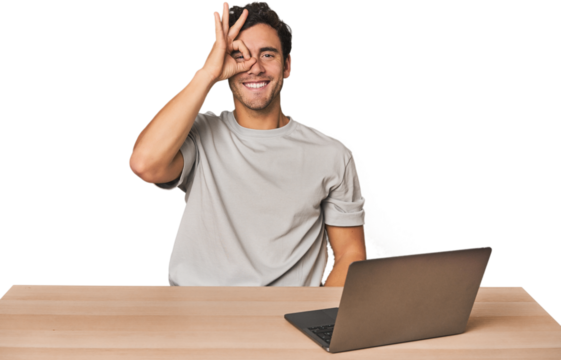 Hispanic young man working on laptop excited keeping ok gesture on eye.
