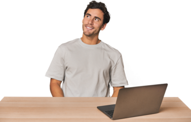 Hispanic young man working on laptop relaxed and happy laughing, neck stretched showing teeth.