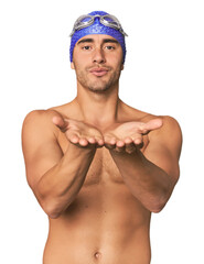 Young Hispanic man with swim gear folding lips and holding palms to send air kiss.