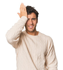 Young Hispanic man in studio forgetting something, slapping forehead with palm and closing eyes.