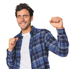 Young Hispanic man in studio celebrating a special day, jumps and raise arms with energy.