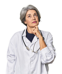 Caucasian mid-age female doctor with stethoscope looking sideways with doubtful and skeptical...