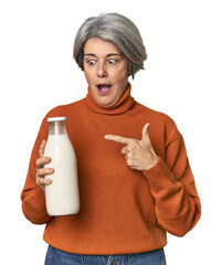 Caucasian mid-age female holding milk bottle pointing to the side