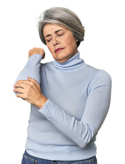 Caucasian mid-age female on studio background massaging elbow, suffering after a bad movement.