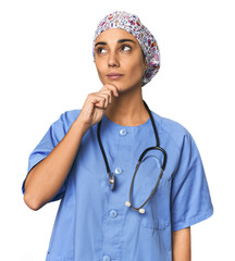 Hispanic nurse in uniform with stethoscope looking sideways with doubtful and skeptical expression.