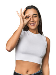 Hispanic young woman excited keeping ok gesture on eye.