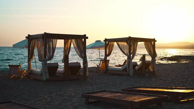 Beach cabana beds and sun loungers on the seashore at sunset.