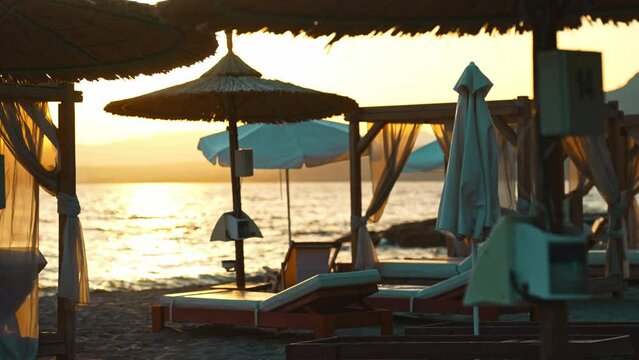 Beach cabana beds and sun loungers on the seashore at sunset.