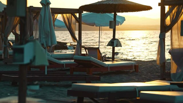 Beach cabana beds and sun loungers on the seashore at sunset.