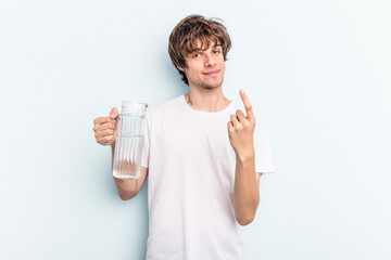 Young caucasian man holding a jar of water isolated on blue background pointing with finger at you...