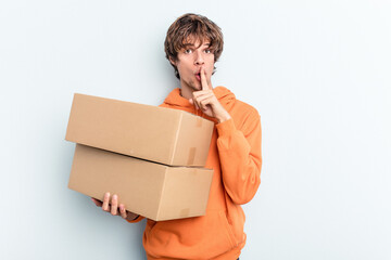 Young man making a move while picking up a box full of things isolated on blue background keeping a...