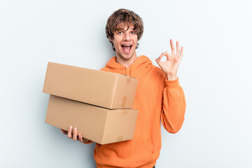 Young man making a move while picking up a box full of things isolated on blue background cheerful...