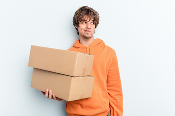 Young man making a move while picking up a box full of things isolated on blue background confused,...
