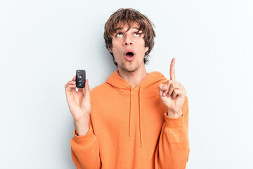 Young caucasian man holding car keys isolated on blue background pointing upside with opened mouth.