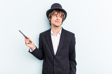 Young magician man holding magic cards isolated on blue background dreaming of achieving goals and...