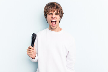 Young caucasian singer man isolated on blue background screaming very angry and aggressive.