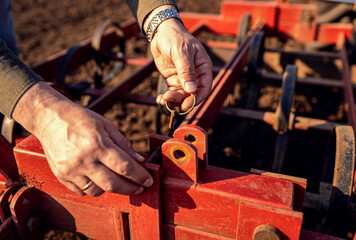 Close up of farmer hands in field preparing the harrow for cultivating the land.