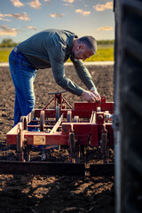 Portrait of farmer standing in field preparing harrow to cultivate the land with a tractor.