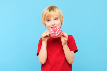 Cute little boy with blond hair and freckles eating a glazed donut. Boy holding colorful donuts,...