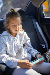 Young Girl Engrossed in Using a Smartphone While Sitting in a Car on a Sunny Day