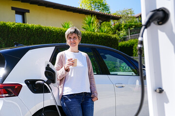 Casual moment as a woman enjoys her coffee next to a charging EV.