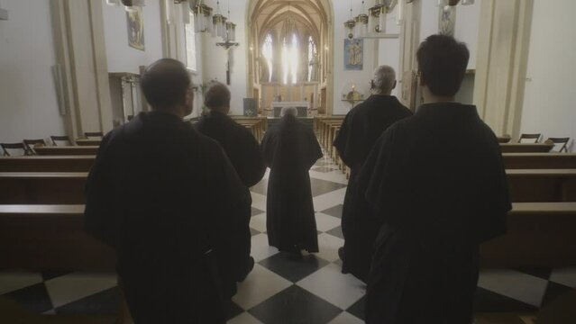 Christian monks in robes walking through aisle to altar in church back view tracking shot. Prayers religious procession. Christianity concept