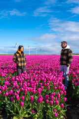 Two men standing tall in a sea of vibrant purple tulips, surrounded by windmill turbines in the Dutch countryside during Springtime