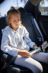 Young Girl Engrossed in Using a Smartphone While Sitting in a Car on a Sunny Day