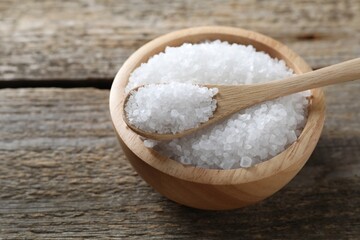 Organic salt in bowl and spoon on wooden table, closeup. Space for text