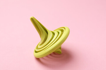 One green spinning top on pink background, closeup