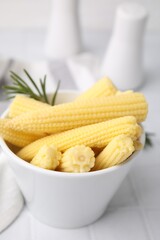 Tasty fresh yellow baby corns in bowl on white tiled table, closeup
