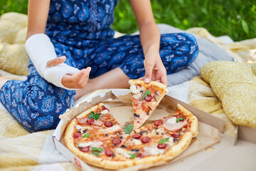 Young Girl With Broken Arm Enjoying Pizza in Sunlit Garden