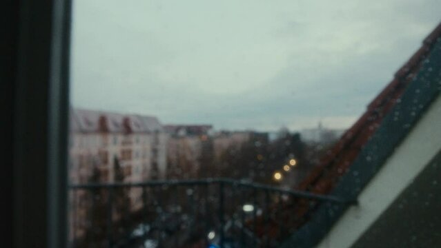 City being seen by someone in a window, the camera refocus to show  the drops of rain in the window