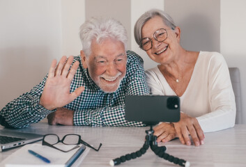 Video call concept. Elderly couple sitting at home talking remotely with family or friends on...