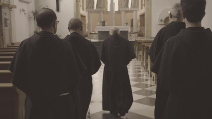 Christian priests walking along church pew rows aisle back view tracking shot. Monks waring robes moving to altar in temple. Christianity concept
