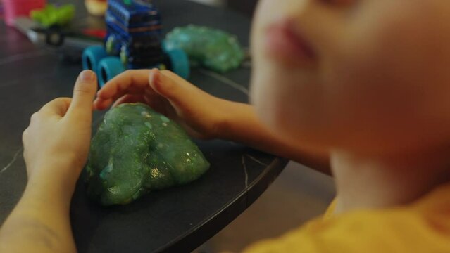 Close-up view of a child's hands crumpling slime making green glitter homemade slime.