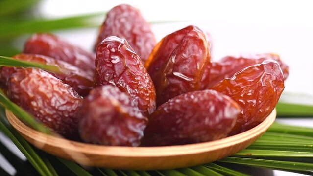 Dates fruit. Date fruits in wooden bowl with palm tree leaf isolated on white background. Medjool dates close up. Slow motion. 