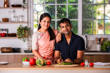 Indian happy young couple preparing food in kitchen together