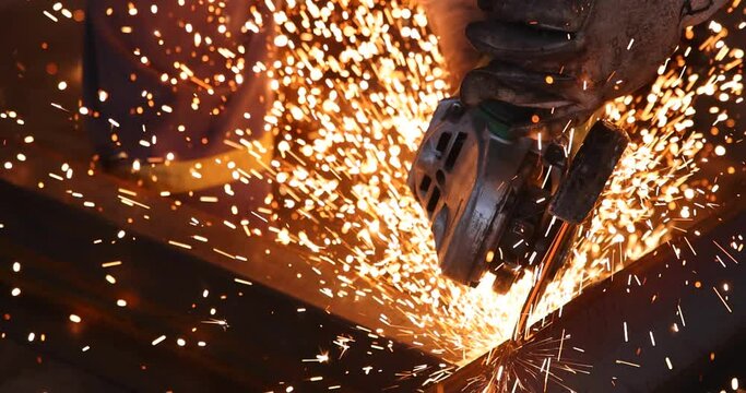 Steel worker grinding a metal construction with grinder in the factory, close up slow motion